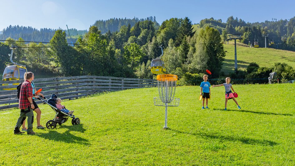 Familie mit Kinderwagen und Kindern vor Disc-Golf Korb